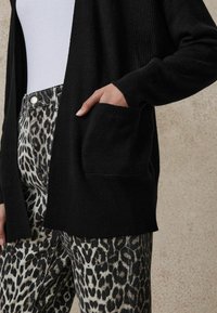Svart ribbade cardigan med öppen front och sidofickor, ihop med beigefärgade leggings med svart leopardmönster.