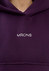 Felpa viola con cappuccio, caratterizzata da un logo ricamato bianco "MÍRONS" sul davanti. Il materiale sembra morbido con una texture liscia.