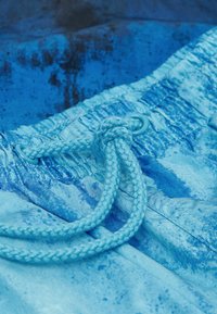 Bañador de color azul claro con una tela texturizada, cierre con cordón, ojales reforzados y un patrón similar a una acuarela en todo el material.