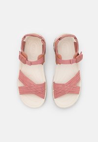 Vaaleanpunaiset ja beige sandaalit, joissa on joustavat ristitaskuin koristellut hihnat, pehmustettu valkoinen pohja ja säädettävä nilkkahihna.