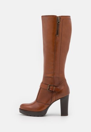 Botte haute en cuir marron jusqu'au genou avec un bout arrondi, une fermeture éclair latérale et une sangle bouclée. Talon haut et solide avec une semelle en caoutchouc texturé.