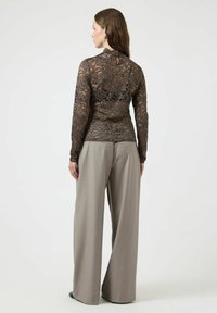 Brun bluse av blonder med lange ermer og høy hals, kombinert med vide grå bukser. Teksturert blonde med blomsterdesign.