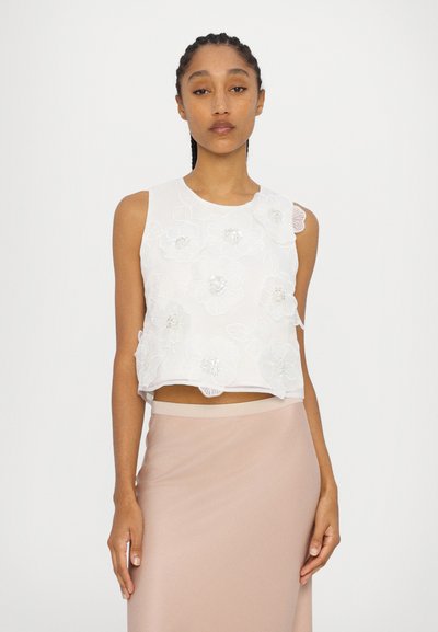 Weißes ärmelloses Top mit floralem Stickmuster, das ein kurzes Design und subtile Texturdetails aufweist; kombiniert mit einem hellrosa Rock.
