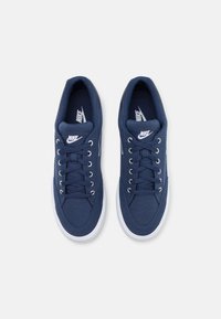 Námořnické modré plátěné tenisky s bílými tkaničkami, gumovými podrážkami a stříbrnými očky. Na jazyku a boku mají logo Nike. Hladký texturovaný povrch.