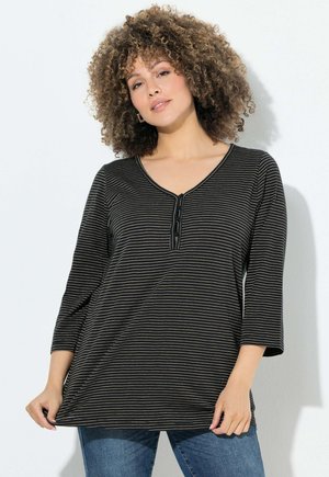 Haut à rayures noir et crème à manches longues avec un décolleté en V et une patte de boutonnage à quatre boutons. Tissu doux avec une coupe décontractée, associé à un jean bleu.