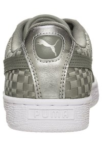 Sneakers PUMA z szarym plecionym tekstylnym wierzchem, srebrnymi akcentami, miękkim wykończeniem kołnierza i białą gumową podeszwą z fakturowanym wykończeniem.