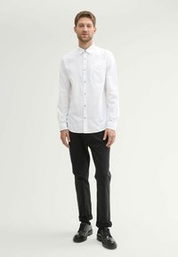 Witte langesleeve overhemd met knopen en een zak, gecombineerd met zwarte broek en zwarte leren schoenen. Het overhemd heeft een klassieke kraag en knoopdetails.