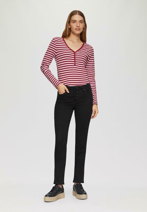 Rood-wit gestreepte longsleeve top met een V-hals en knoopdetails, gecombineerd met zwarte slim-fit jeans en zwarte platform sneakers.