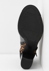 Musta nahkasaapas, jossa on teksturoitu kumipohja. Sivussa on leopardi-printtiakseli, jossa on vaakaompeleita.