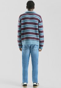 Sweter w paski w kolorach bordowym i jasnoniebieskim, o puszystej fakturze i luźnym kroju, zestawiony z jasnoniebieskimi dżinsami i tenisówkami.