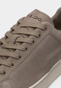 Baskets en daim taupe avec lacets plats assortis, œillets ronds, détails surpiqués et "ALDO" embossé sur la languette au-dessus de la semelle en caoutchouc crème.