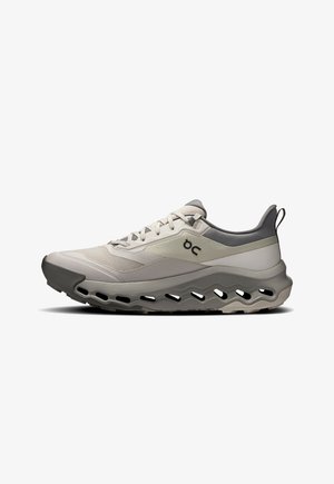 Chaussure de course légère en beige et gris. Elle présente une tige en mesh respirant, une semelle extérieure épaisse avec découpes et un col rembourré.