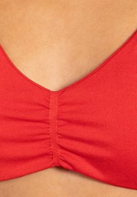 Top de bikini rojo con escote en V profundo, tejido recogido en el centro y textura suave. Las tiras son finas y ajustables.