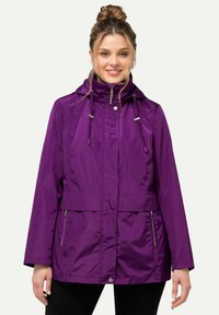 Lila vattentät jacka med huva, dragkedjefickor, justerbara dragsnoddar vid halslinningen och en avslappnad passform. Slät, glänsande tyg.