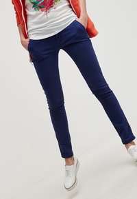 Marinblå, slim-fit byxor i lätt bomull, med sidfickor och en slät yta. Kombination med en vit skjorta och ljusa skor.