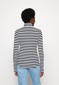 Black and white striped long-sleeve top with a high collar. Ribbed texture. Styled with light blue jeans.