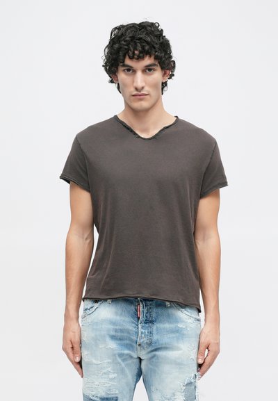 T-shirt de manga curta cinza escuro com decote cru e um discreto detalhe de botão. Usado com jeans claros desgastados. Textura de tecido suave.