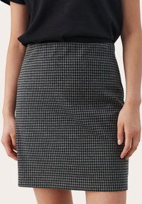 Jupe crayon noire et blanche à carreaux, avec une texture lisse et une coupe ajustée, se terminant au-dessus du genou. Style minimaliste sans matériel visible.