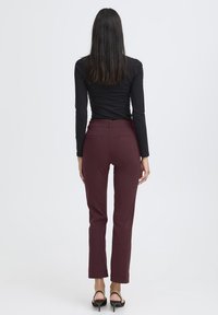 Bordeaux broek met een slim fit, voorzien van achterzakken en een normale taille, gecombineerd met een zwarte langemouwen top en zwarte hakken.