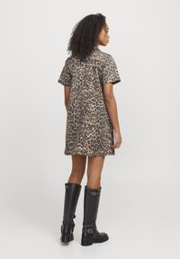 Vestido de leopardo con mangas cortas, corte recto y botones en la espalda. Llevado con botas altas de cuero negro con hebillas.