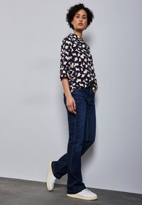 Camicia a righe blu navy e crema con colletto e maniche 3/4, abbinata a jeans blu scuro e sneakers bianche. Design minimalista.