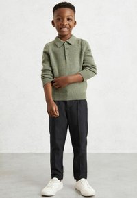 Zöld kötött pulóver gallérral, fekete keskeny nadrág és fehér sportcipő. Az anyag texturált, látható varrásokkal.