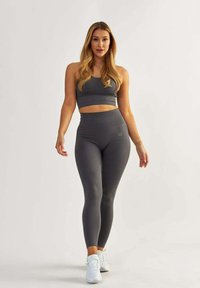 Harmaa urheilullinen crop-top ja korkea vyötärö leggings, kammatut pinnat, joissa on hienovarainen brändäys. Mallilla on valkoiset urheilukengät.