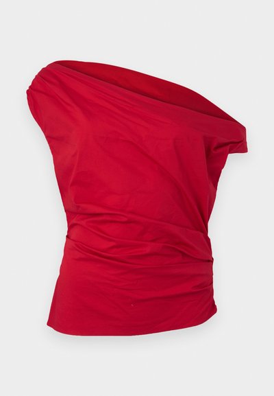 Κόκκινο ασύμμετρο τοπ χωρίς μανίκια με draped ύφασμα και σούρα στη μέση, εμφανίζεται σε απλό ανοιχτό γκρι φόντο.