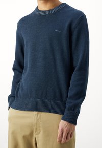 Marineblauer Strickpullover mit einem gerippten Rundhalsausschnitt und einem gerippten Saum, der subtile kontrastierende Sprenkel im gesamten Stoff aufweist.