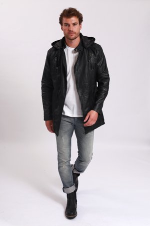 Chaqueta de cuero negra con capucha, que cuenta con bolsillos con cremallera y acentos acanalados en los hombros. Llevada sobre una camisa blanca, combinada con jeans claros y botas.