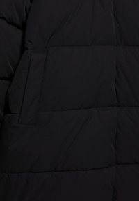 Schwarze Daunenjacke mit gestepptem Design, sichtbaren Nähten und einer Seitentasche. Das Material wirkt weich und glatt in der Textur.