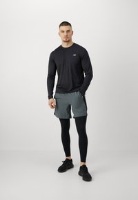 Fekete hosszú ujjú felső, szürke rövidnadrág és fekete leggings. A felsőn egy kis logó található; a rövidnadrág könnyű, laza szabású.