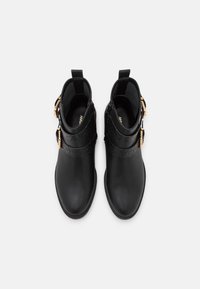 Botas negras hasta el tobillo con un acabado suave, que presentan correas decorativas y acentos de hardware dorado. Incluyen una cremallera para ponerlas y quitarlas fácilmente.