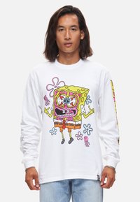 Biała koszula z długim rękawem z kolorową grafiką kreskówkowego SpongeBoba z wyolbrzymionymi cechami, obok różowych meduz i kwiatów.