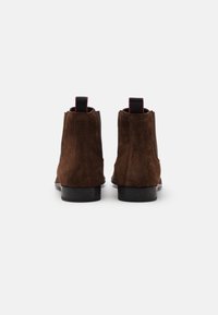 Bottes chevilles en daim brun à finition lisse, dotées de panneaux latéraux élastiques et d'une languette à l'arrière, reposant sur un talon empilé noir.