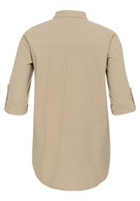 Chemise beige à manches longues avec col, offrant des manches retroussables, un ourlet légèrement arrondi et un pli dans le dos pour le confort. Texture de tissu lisse.