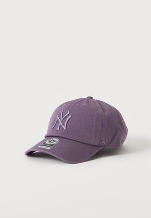 Fioletowa czapka z daszkiem z wyszywanym logo New York Yankees na przodzie i zakrzywionym daszkiem, leżąca na białej, gładkiej powierzchni.