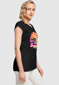 Svart T-skjorte med korte ermer, med et fargerikt palmetrædsdesign og teksten "Summer Vibes" i rosa og grønt, avslappet passform.