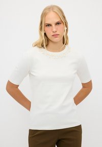 Vit stickad kortärmad topp med rund hals dekorerad med små beige pärlliknande detaljer. Slät textur, smal passform.