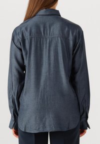 Diepblauw, overhemd met lange mouwen van een gladde stof, met een subtiel stippenpatroon en geknoopte manchetten. De achterkant toont details van een schouderstuk en plooien.