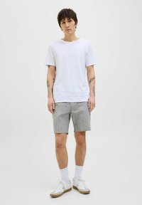 White short-sleeved t-shirt paired with light gray shorts. The model wears white sneakers with tan accents and ankle socks.