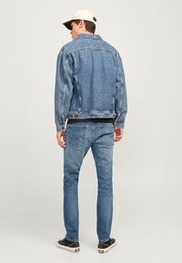 Denim jakna svijetloplave boje s opuštenim krojem, džepovima s našivkom i iznošenim detaljima, u kombinaciji sa skinny trapericama i crnim tenisicama.