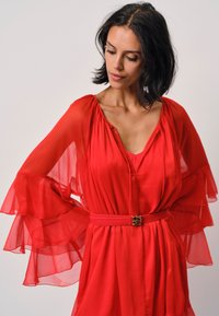 Rotes Chiffonkleid mit fließenden Glockenärmeln, tiefem V-Ausschnitt und einem taillierten Gürtel mit einer dekorativen goldenen Schnalle.