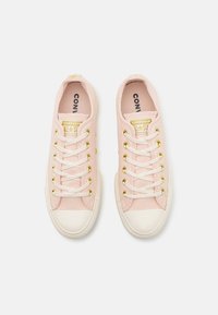 Světle růžové plátěné tenisky s bílou gumovou špičkou a zlatými očky. Obsahují bílé tkaničky a logo "CONVERSE ALL STAR" na jazyku.