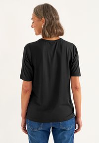 Sort kortærmet T-shirt med rund halsudskæring, der har en blød tekstur og en afslappet pasform, båret med blå jeans.
