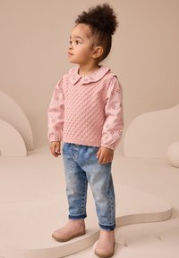 Lyserød strikket sweater med diamantmønster og krave, kombineret med lyseblå jeans og lyserøde ankelstøvler med blomsterdetaljer.