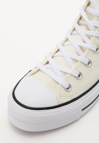 Canvas sneakers med krämfärgad ovandel, vita snören och svart gummisula. Har en rund tå och silverfärgade öglor. Texturerad gummiyttersula.