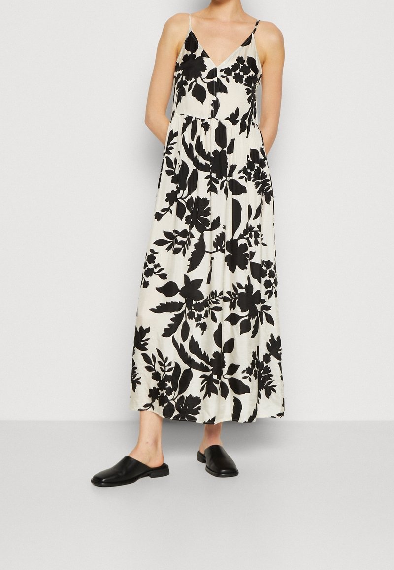 Maxiklänning med svart blommönster på vit bakgrund. Har V-ringning, spaghettiband och en luftig silhuett. Matchas med svarta mules.