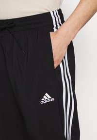 Melnas sporta šortus ar teksturētu audumu, ar baltām sānu svītrām un Adidas logo izšūtu kreisajā pusē. Ar aukliņu regulējama josta.