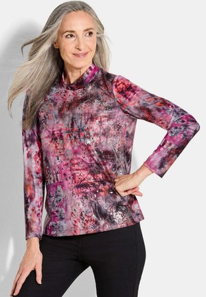 Langärmlige Bluse in Lila und Pink mit Muster, featuring einen hohen Kragen und einer Mischung aus abstrakten Texturen und metallischen Akzenten.